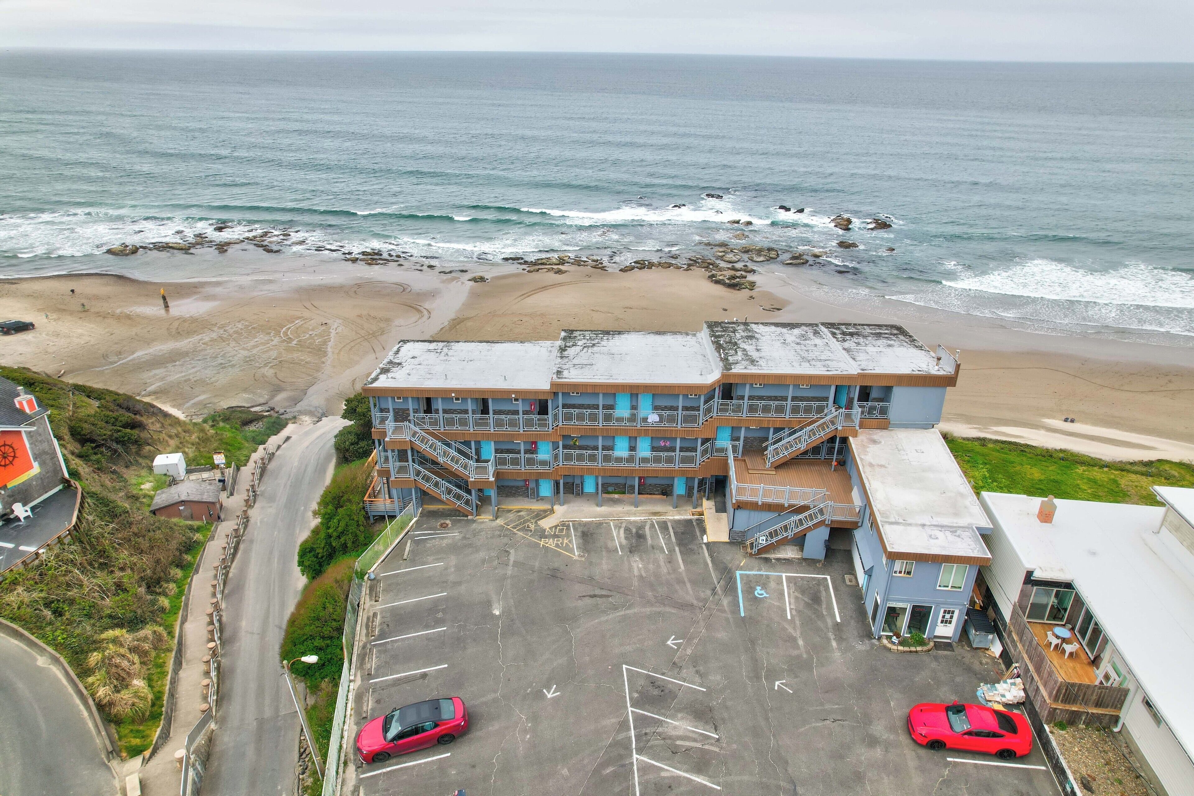 Un bâtiment avec un parking, une plage et l’océan en arrière-plan.