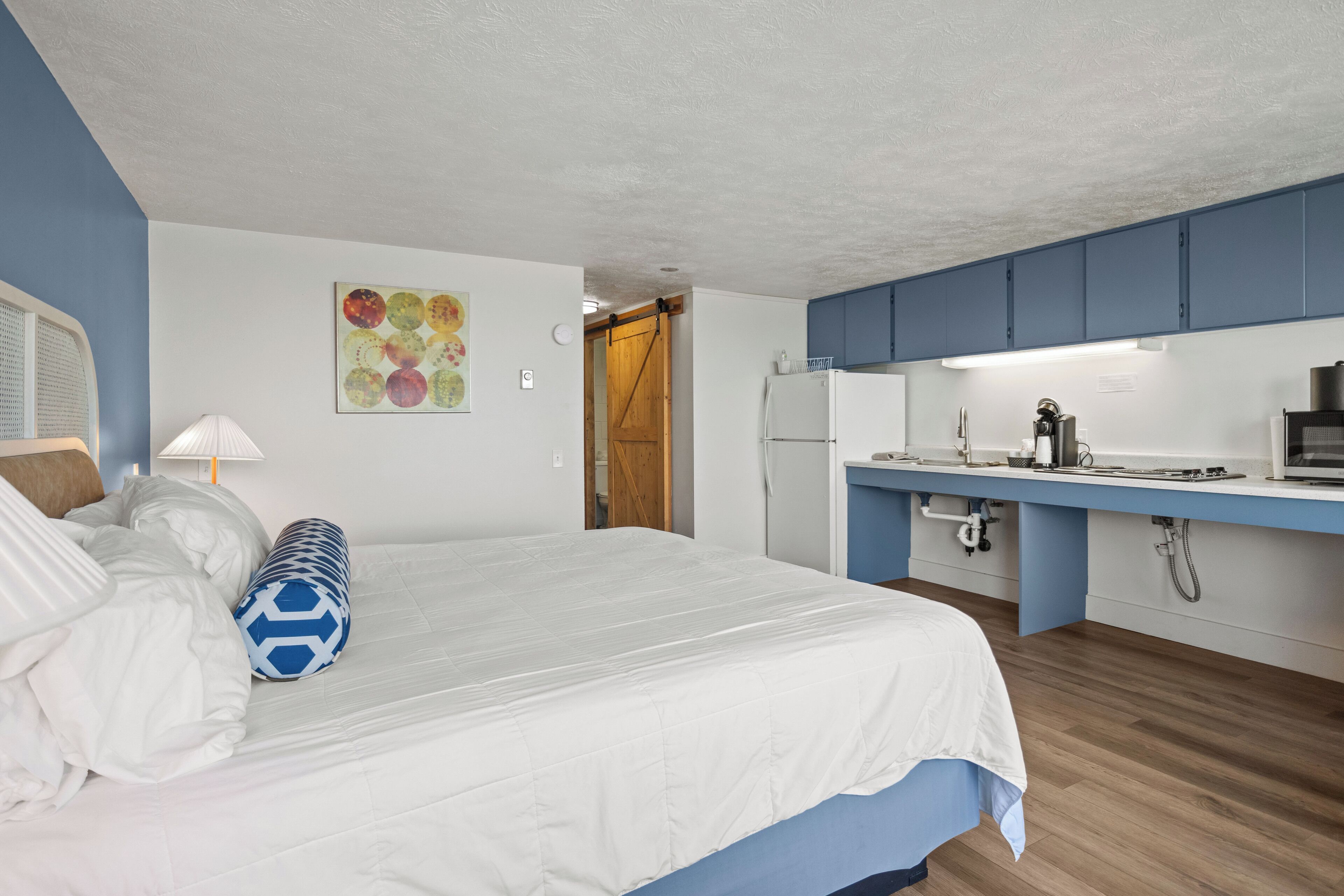 A bedroom with a bed, a desk, and a kitchenette.