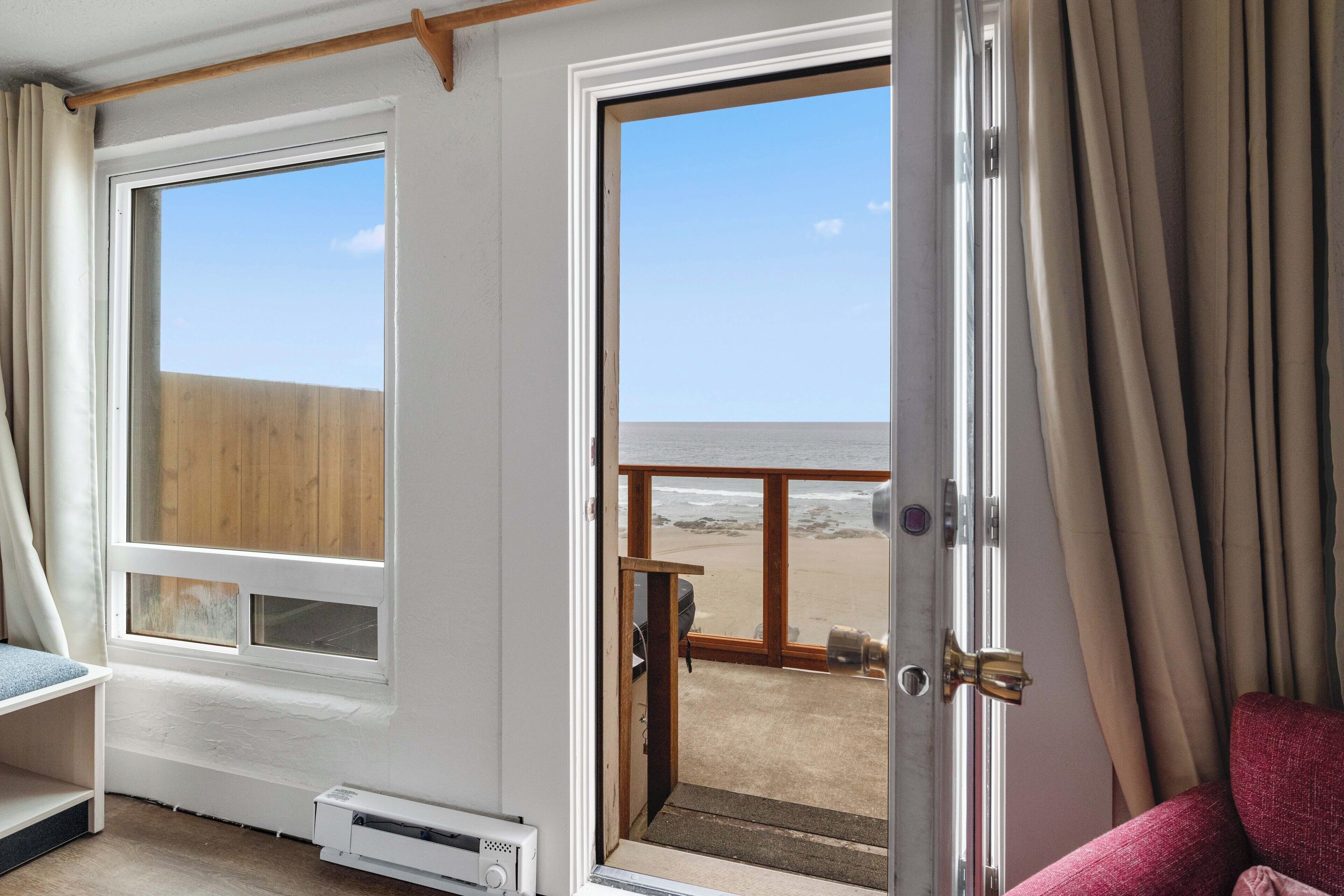 Een kamer met een groot raam en een deur naar een balkon met uitzicht op het strand.