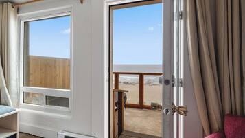 Een kamer met een groot raam en een deur naar een balkon met uitzicht op het strand.
