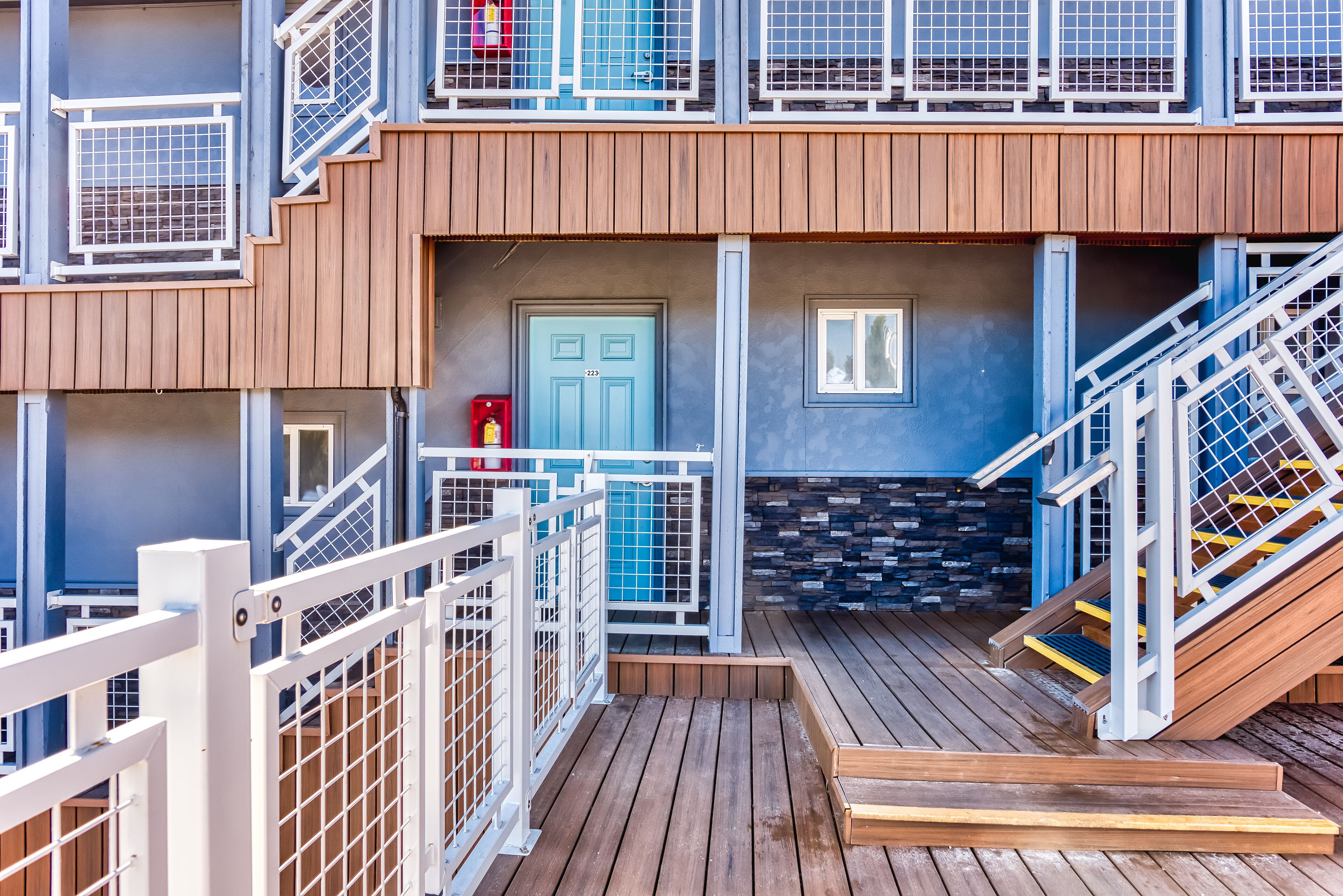 A multi-level building with wooden deck areas, metal railings, and a blue door.