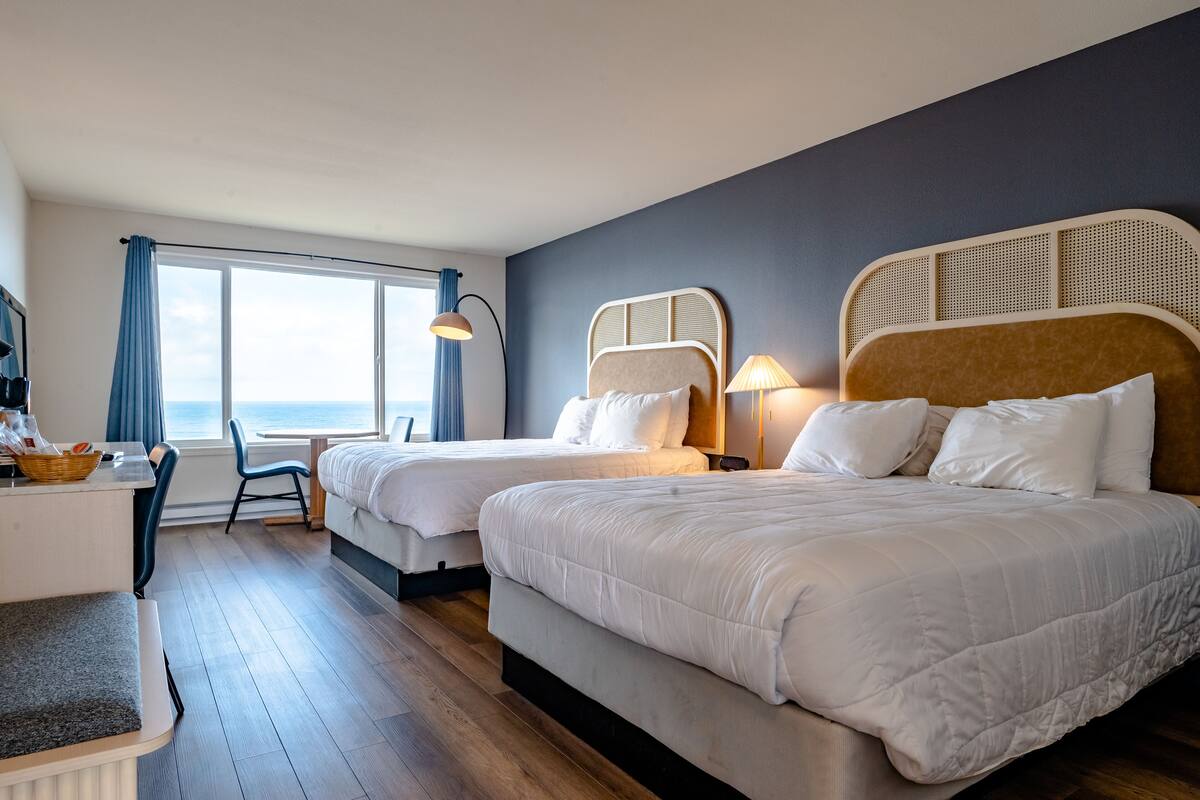 Een hotelkamer met twee bedden, een bureau en uitzicht op zee.