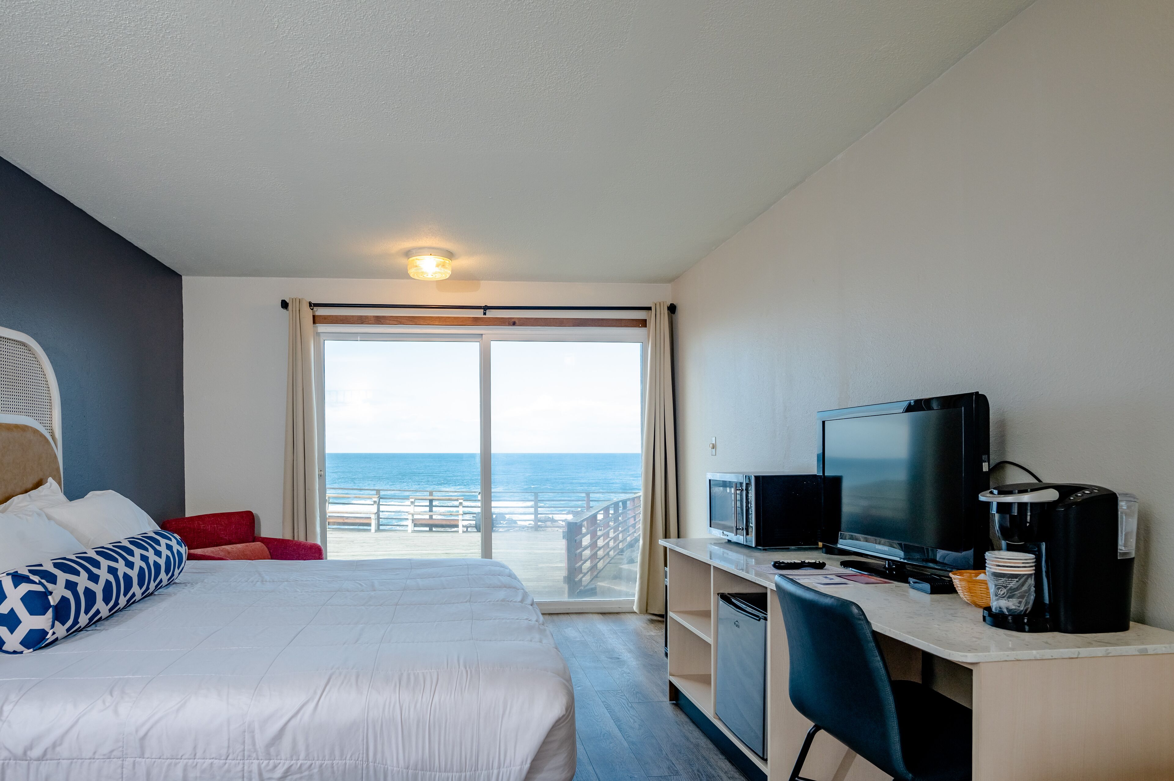 Une chambre d’hôtel avec un lit, un bureau avec une télévision, une machine à café et une vue sur l’océan.