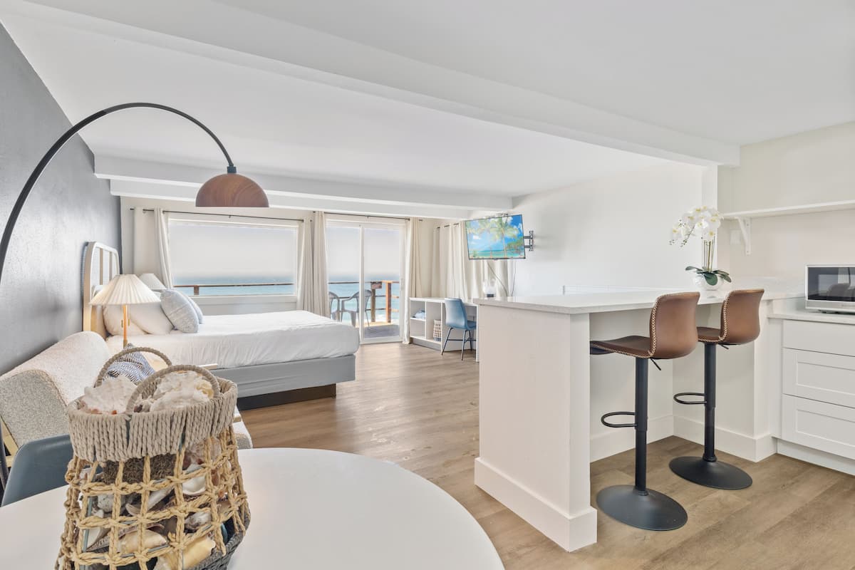 Een moderne hotelkamer met een bed, een zithoek met barstoelen, een televisie en uitzicht op zee.
