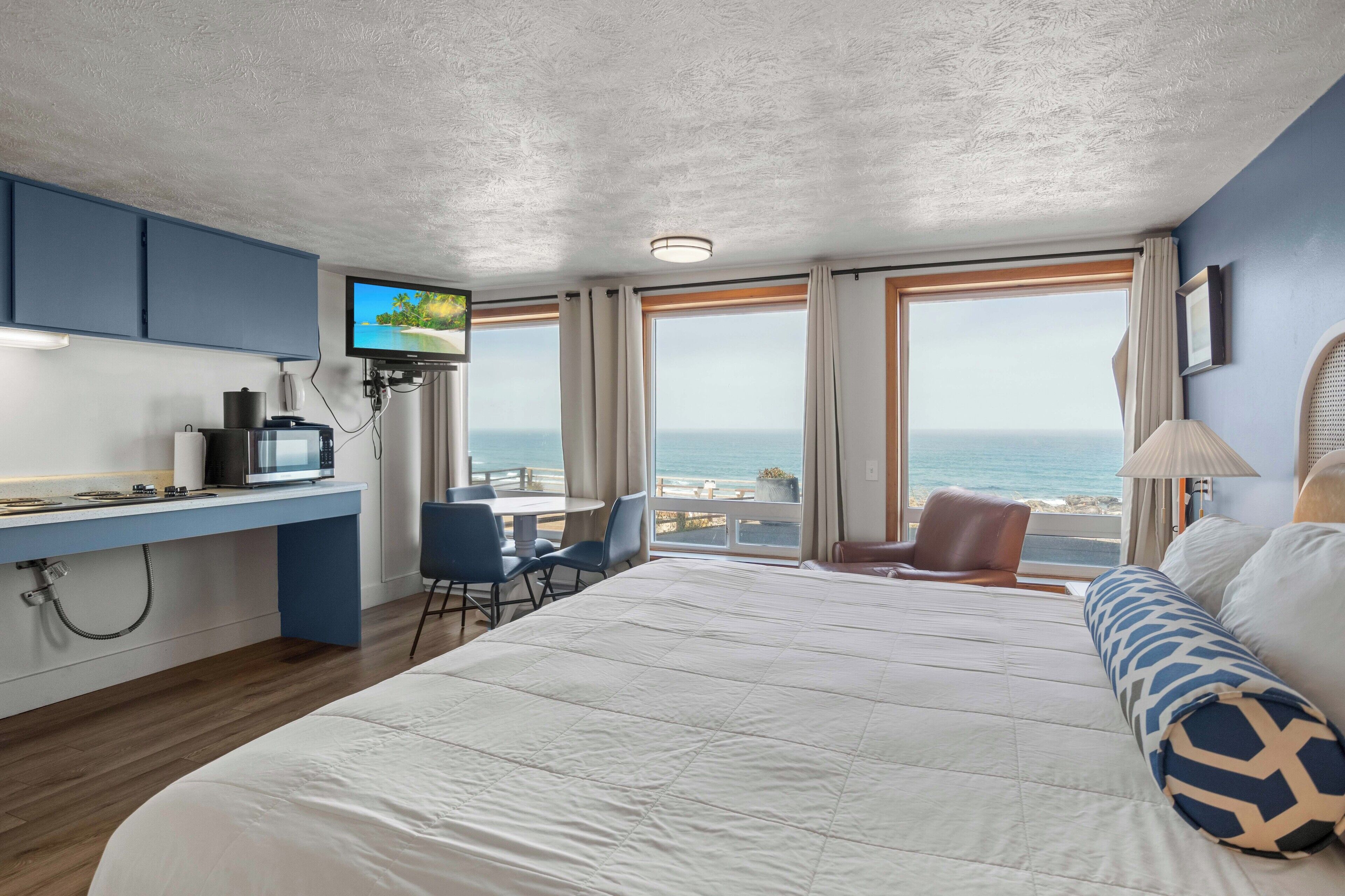 A hotel room with a bed, a desk with a TV, a view of the sea, and a chair.