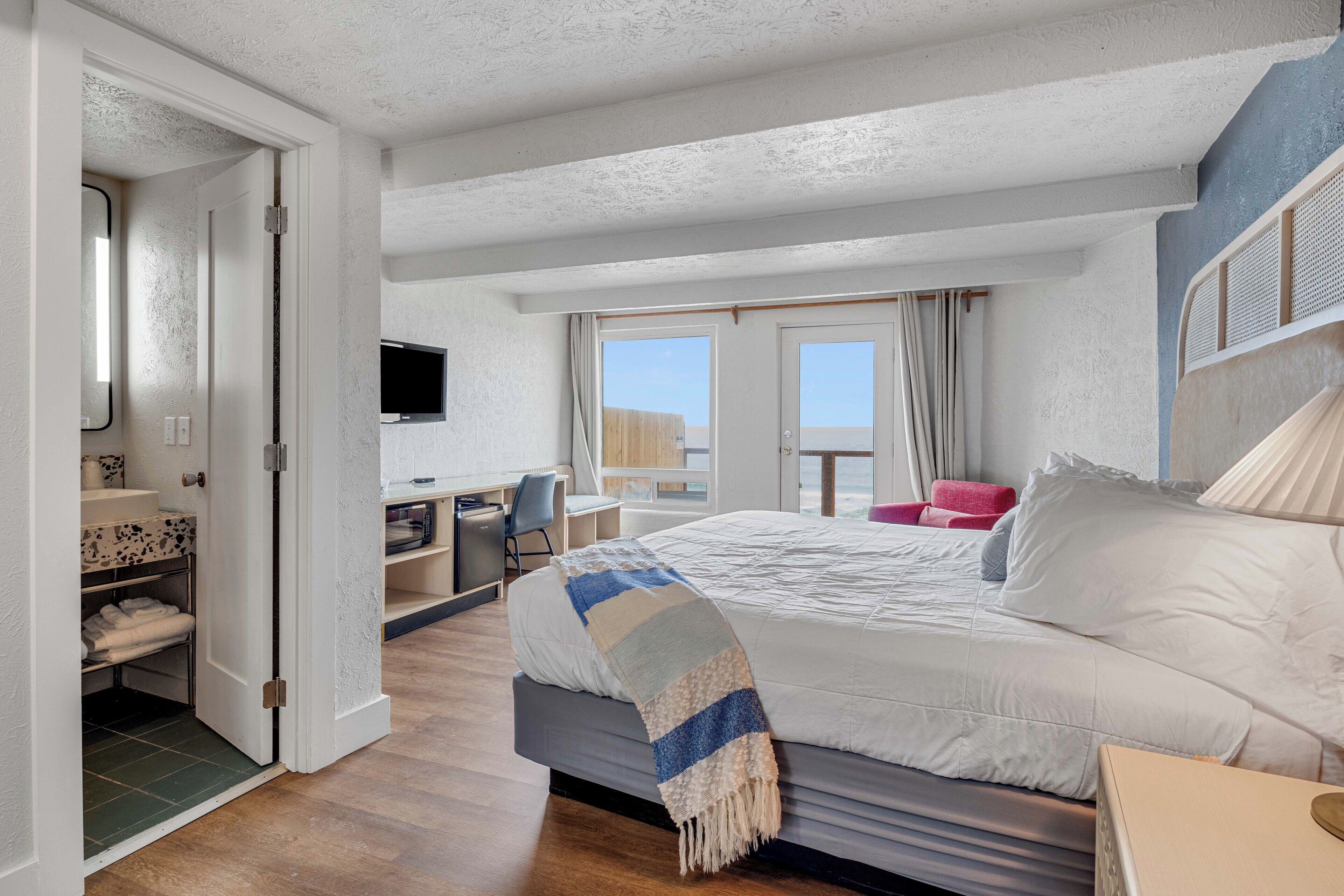 Une chambre d’hôtel équipée d’un lit, d’un bureau, d’une chaise, d’une télévision et d’un balcon avec vue.