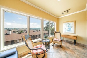 A sunlit room with large windows, wicker furniture, and a view of buildings.