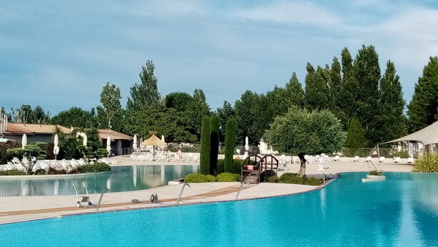 A large, clear swimming pool with lounge chairs and umbrellas, surrounded by trees and buildings. - Vias Plage,la Carabasse Mobil Home Tout Confort (Vias-plage)