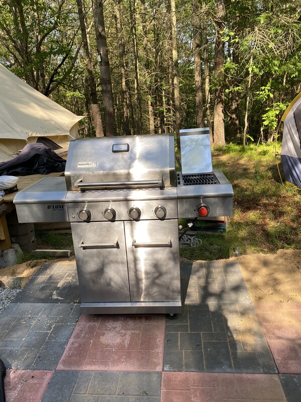 En transportabel grill med en bærbar computer ovenpå, placeret i et skovområde med et telt i baggrunden.
