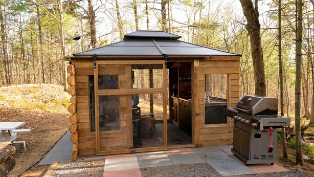 A wooden cabin with a grill and a picnic table outside.