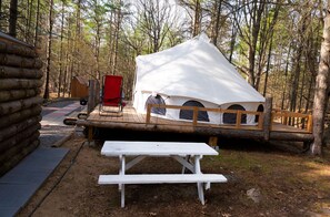 A rustic cabin with a wooden deck, a picnic table, and a red chair.