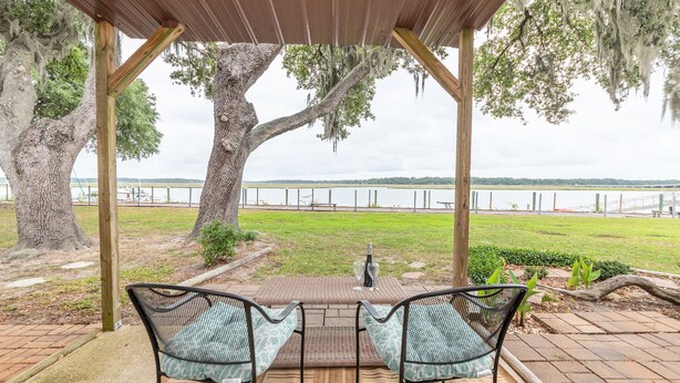 Un patio couvert avec deux chaises et une table, donnant sur un lac, avec une clôture en arrière-plan.