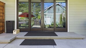 A front door with a glass panel, a wooden door frame, a black mat, and a small wooden box. - Luxury CDA home walk to lake with hot tub (Coeur d'Alene)