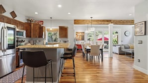 A modern kitchen with a central island, bar stools, and a dining area with a view of the outdoors. - Luxury CDA home walk to lake with hot tub (Coeur d'Alene)