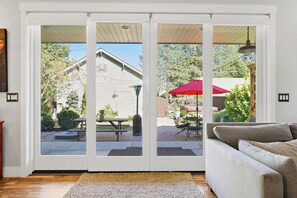 A room with a sliding glass door leading to an outdoor patio area with a table and chairs, a red umbrella, and a garden view. - Modern CDA Retreat Walk to Lake and Hot Tub (Coeur d'Alene)