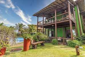 Um edifício de dois andares com varanda de madeira, piscina e vegetação exuberante.