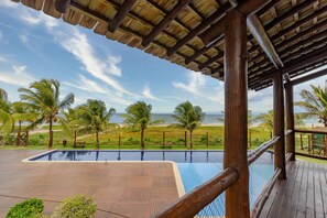 Um deck de madeira com piscina, palmeiras e vista para a praia e o oceano.