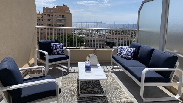 Un balcón con dos sofás y una mesa de centro, con vista a un puerto deportivo con barcos.