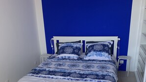 Una cama con estructura blanca y ropa de cama estampada en azul en una habitación con una pared azul y suelo de baldosas.