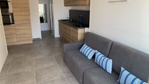 Una cocina moderna con armarios de madera, un sofá gris con cojines a rayas y suelo de baldosas.
