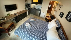 A compact hotel room with a bed, a desk, a TV, a kitchenette, and a small seating area. - Studio Belle Vue Mer (Courseulles-sur-Mer)