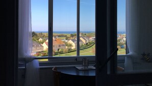 A room with a large window overlooking a residential area and the sea. - Studio Belle Vue Mer (Courseulles-sur-Mer)