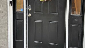 Una puerta negra con el número 631 encima, una corona de hojas verdes y flores rosas, y una ventana pequeña a la izquierda de la puerta.