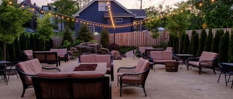 An outdoor patio area with wicker furniture, a stone fire feature, and string lights.