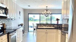 A modern kitchen with white cabinetry, a black countertop, stainless steel appliances, and a large window offering a view of the outdoors. - Located near downtown, restaurants and the beach ! (Naples)