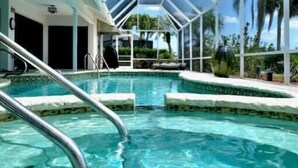 A clear blue pool with a glass ceiling structure, surrounded by palm trees and a clear sky. - Located near downtown, restaurants and the beach ! (Naples)