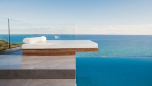 A modern infinity pool with a clear view of the ocean, a white sofa, and a wooden platform. - Luxury fiore suites 3 (Zakinthos)
