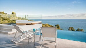 A modern outdoor pool area with a clear view of the sea, a lounge chair, a small table with a drink, and a wooden deck. - Luxury fiore suites 3 (Zakinthos)