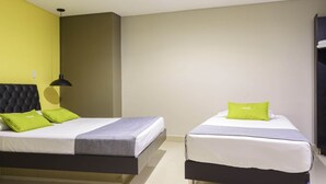 Et hotelværelse med to senge, hver med en grå madras og en grøn pude. Værelset har en guldfarvet væg og en sort sengegavl.