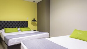 Et hotelværelse med to senge, en sort, betrukken sengegavl og grønne puder.