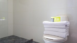 Un baño con azulejos blancos, un inodoro con una pila de toallas blancas y una caja de artículos de tocador Kit sobre el tanque.