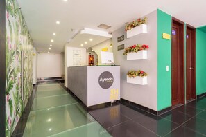 Et hotelreceptionsområde med en receptionsdisk, en grøn væg med blomsterarrangementer og en dør med teksten 'BAJO'.