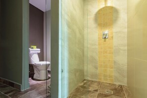 Et badeværelse med toilet, bruseområde med flisebeklædte vægge og et afløb i gulvet.