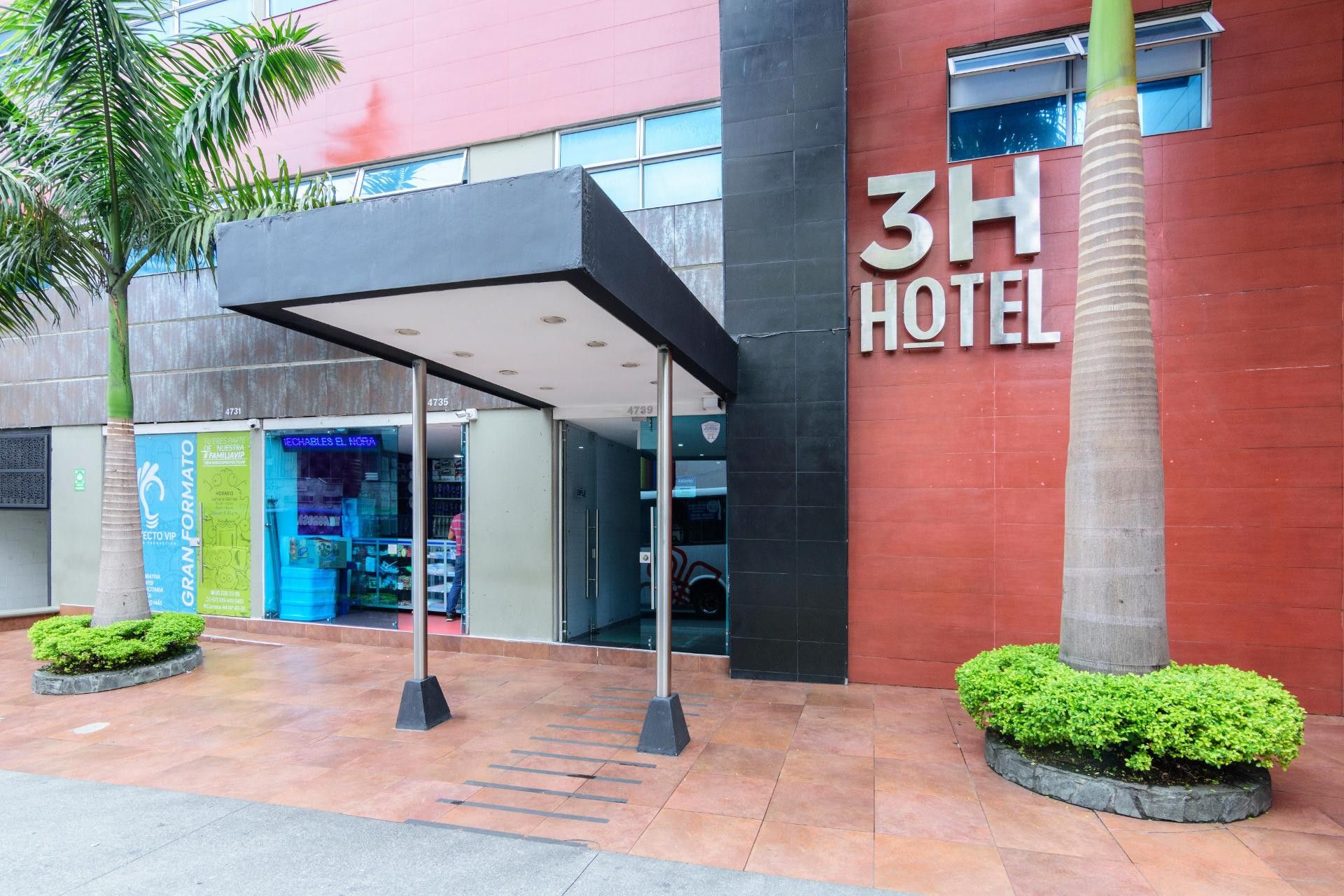 A hotel entrance with a covered walkway, palm trees, and a modern building facade.