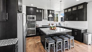 A modern kitchen with dark cabinetry, stainless steel appliances, a granite countertop, and a central island with bar stools.
