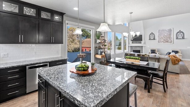 A modern kitchen with dark cabinets, granite countertops, and pendant lighting.