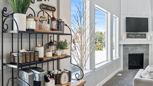 A living room with a fireplace, a coffee machine, and shelves with various items.