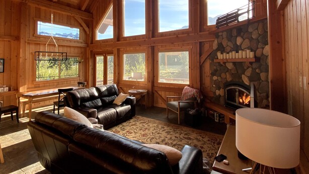 A spacious room with a fireplace, leather sofas, and large windows offering views of the outdoors. - Spacious Luxury View Home: Steps to Hike & Bike, 10pp (Snoqualmie Pass)