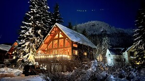 A log cabin with a snow-covered roof, surrounded by snow-laden trees and a mountainous backdrop. - Spacious Luxury View Home: Steps to Hike & Bike, 10pp (Snoqualmie Pass)