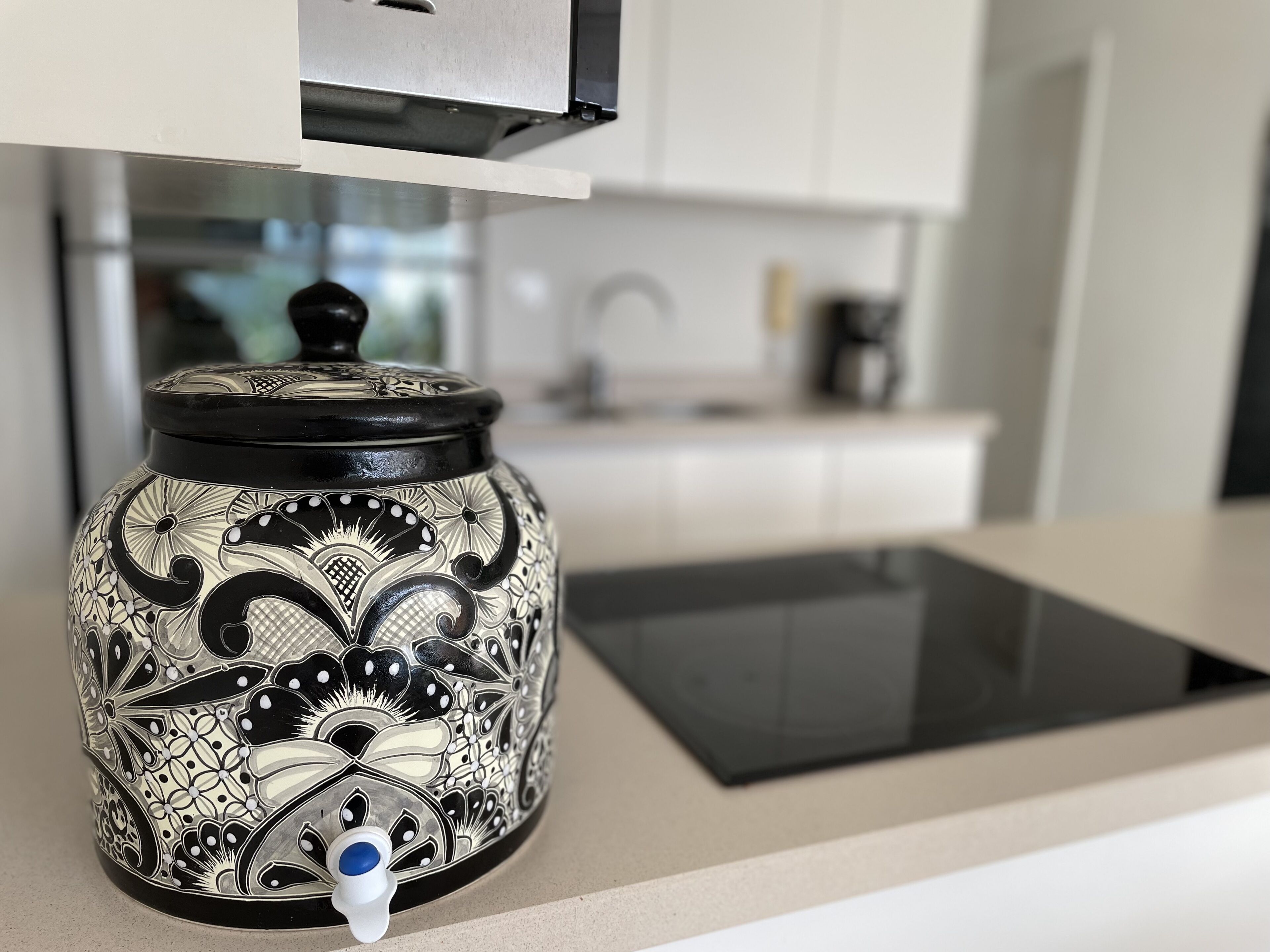 A kitchen with a decorative jar on the counter, a modern stove, and a white cabinet in the background.