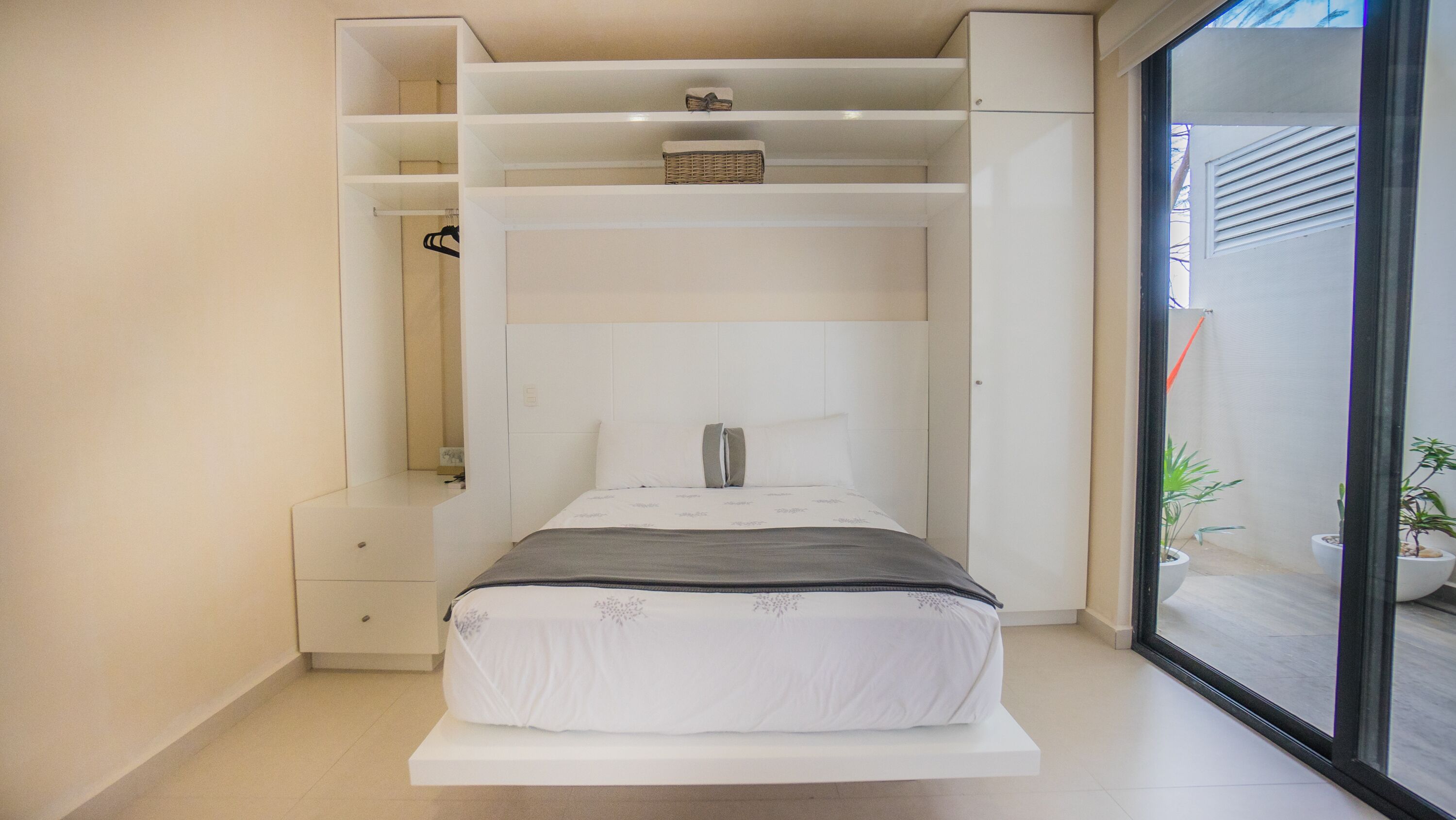 A modern bedroom with a built-in bed, storage shelves, and a sliding glass door to a balcony.