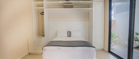 A modern bedroom with a built-in bed, storage shelves, and a sliding glass door to a balcony.