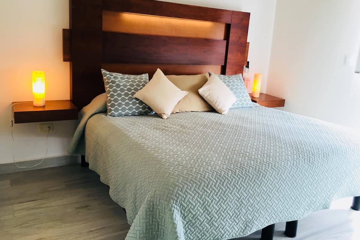 A neatly made bed with a patterned quilt, a wooden headboard, and two bedside lamps.
