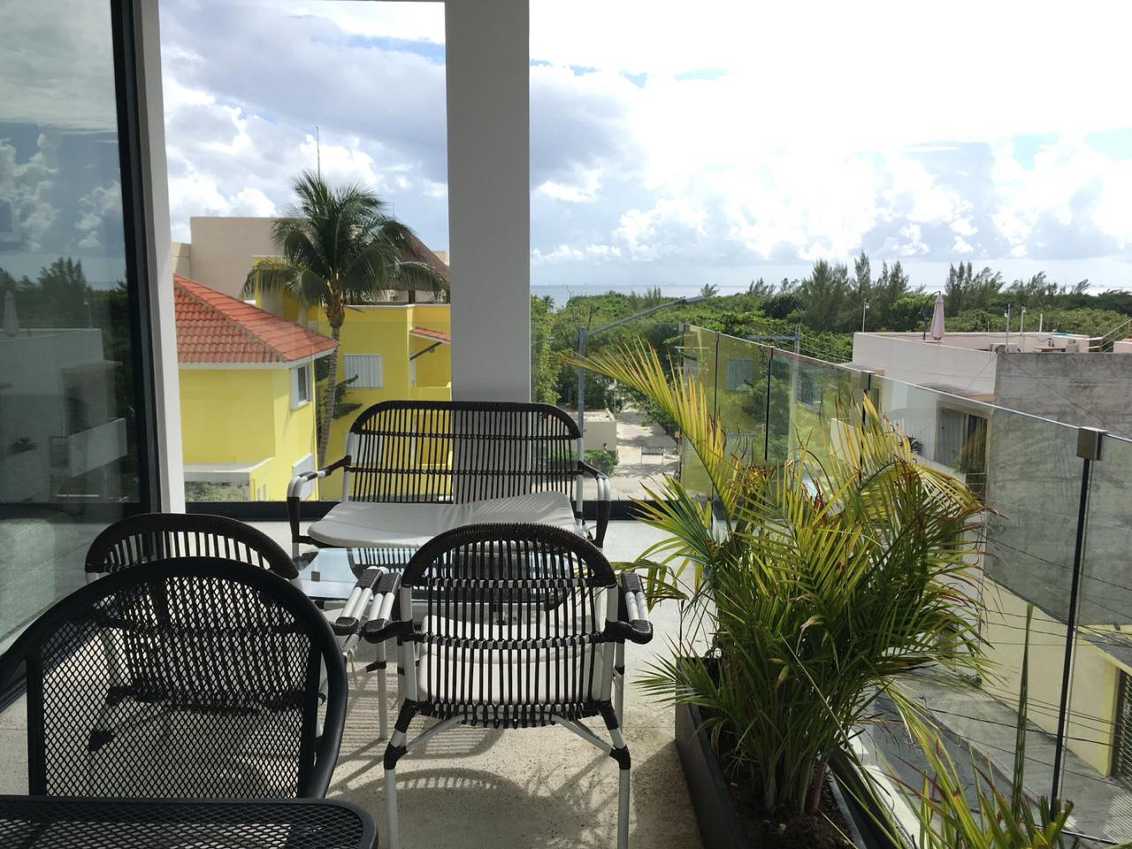 Un balcon avec deux chaises noires et une table, donnant sur un immeuble jaune et sur de la verdure.