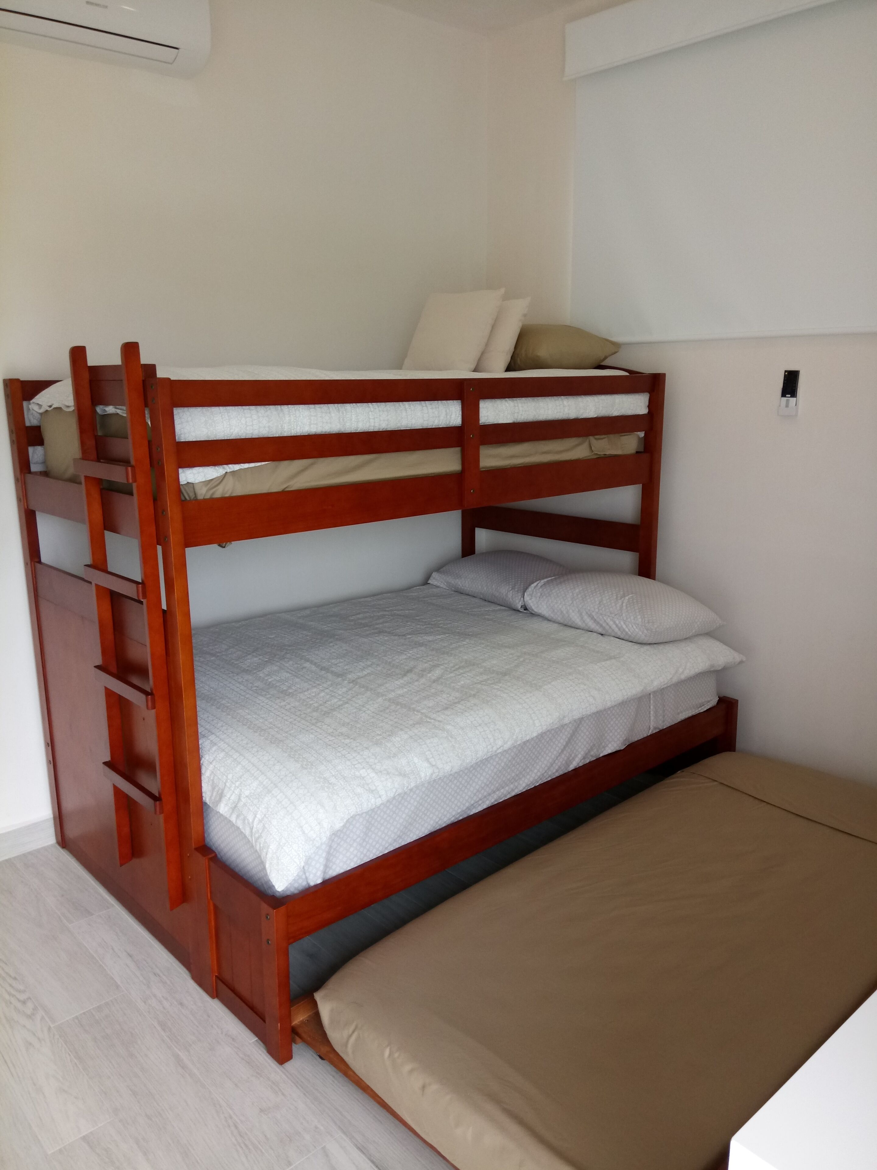 A bunk bed with a wooden frame, a lower bunk with a beige mattress, and a top bunk with a white mattress.