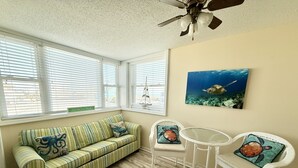 A room with a striped sofa, two chairs, a ceiling fan, and a painting of a sea turtle. - Immaculate two bedroom, two bath oceanview condo located in the heart of North Myrtle Beach!! (North Myrtle Beach)